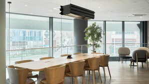 Un salón de conferencias con una larga mesa, varias sillas, una planta en maceta y grandes ventanales que ofrecen vistas de la ciudad.