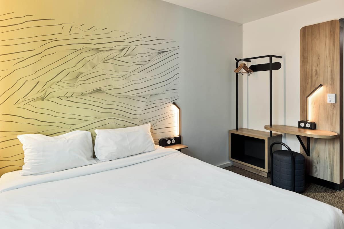 A hotel room with a bed, bedside tables, a wardrobe, and a wall with a textured design.
