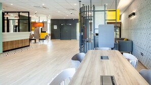Un espacio de oficina moderno con una larga mesa de madera, sillas blancas y una separación con detalles amarillos.