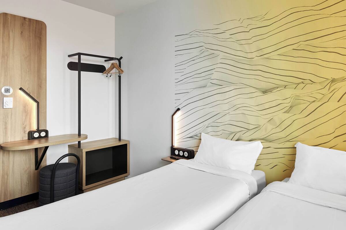Habitación de hotel con cama, mesitas de noche, un escritorio con silla, armario y decoración en la pared.