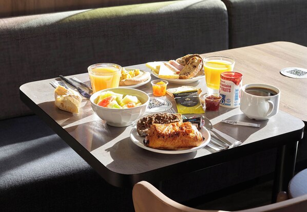 Bandeja de desayuno con tostadas, fruta, jugo y café sobre una mesa en una habitación con un sofá.
