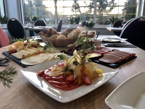 A table with various cheeses, meats, and fruits, arranged on a wooden table in a room with large windows. - Lawendowy Dwór (Pszczolki)