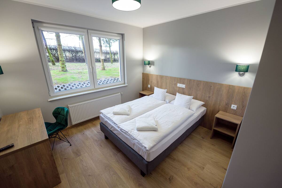 A modern hotel room with a large bed, a desk, and a view of the outdoors.