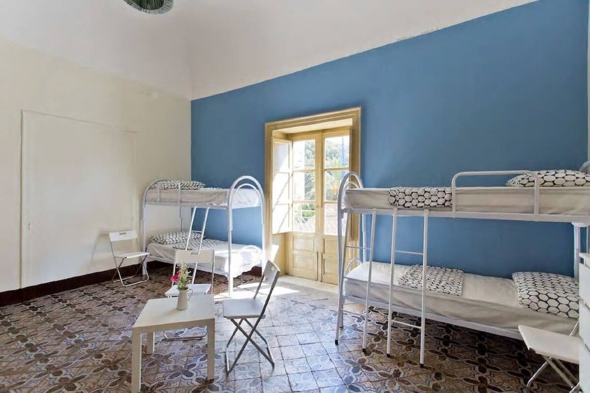 Une chambre avec des lits superposés, une petite table sur laquelle est posé un vase, et une fenêtre donnant sur un paysage verdoyant.