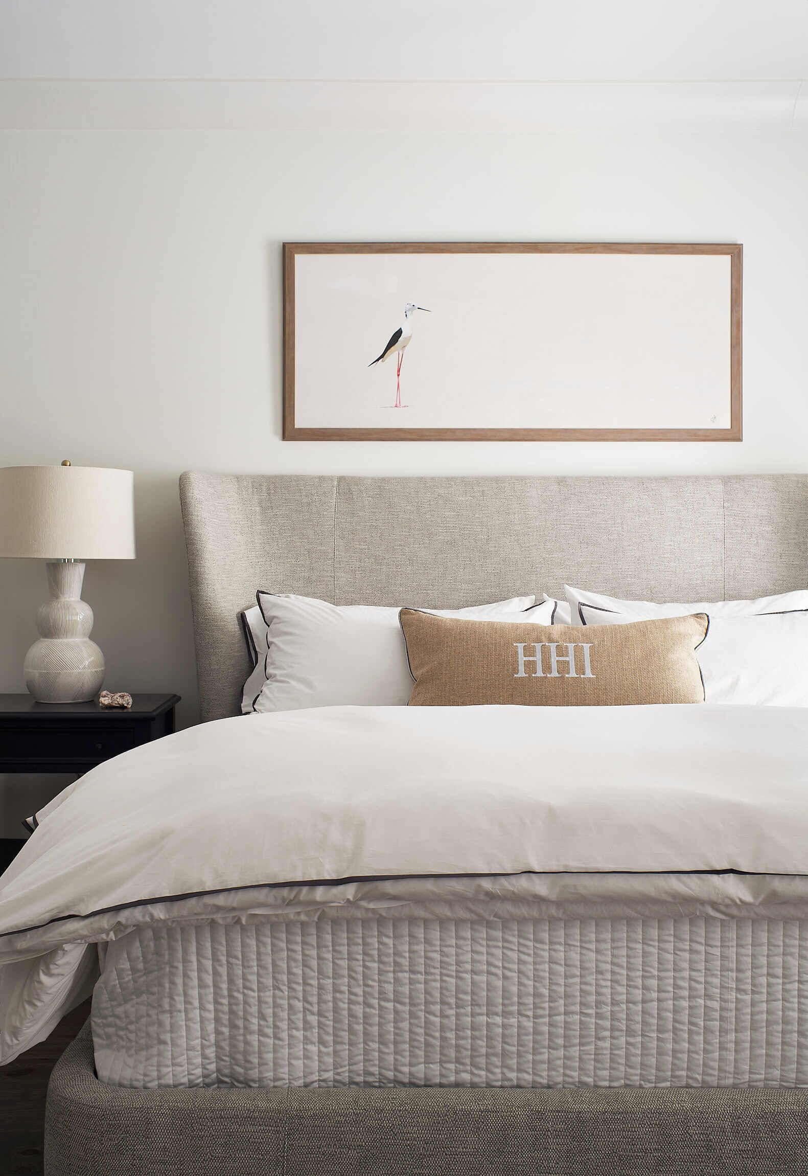 A neatly made bed with a quilted cover, a headboard, and a pillow with 'HHI' embroidered on it.