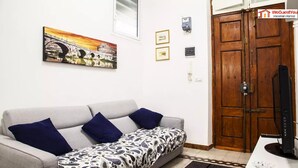 Una sala de estar con un sofá, una televisión, una puerta de madera y un cuadro colgado en la pared.