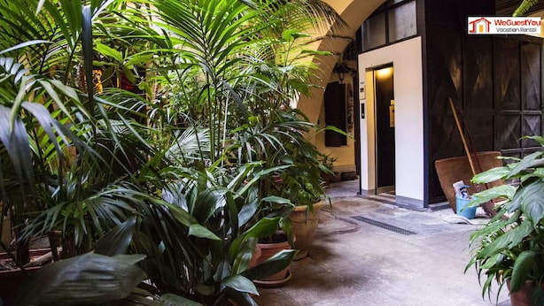 Un patio con plantas en macetas, una puerta que da a una habitación y un cartel que anuncia WeGuestYou Vacation Rental.