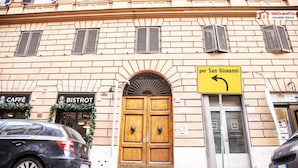 Fachada de un edificio con una puerta de madera, dos escaparates con los rótulos 'CAFFÈ' y 'BISTROT', y un cartel que indica 'per San Giovanni'.