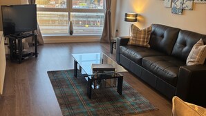 Uma sala de estar moderna com um sofá de couro, uma mesa de centro de vidro e uma TV de tela plana em um suporte.