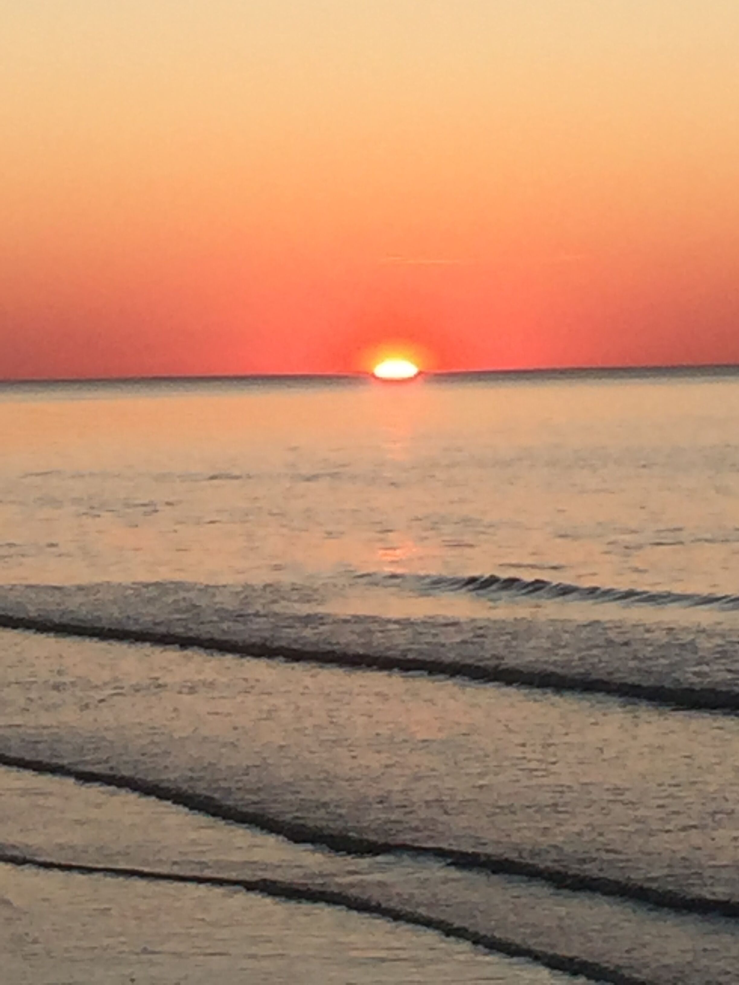 Un coucher de soleil sur une mer calme aux vagues douces.