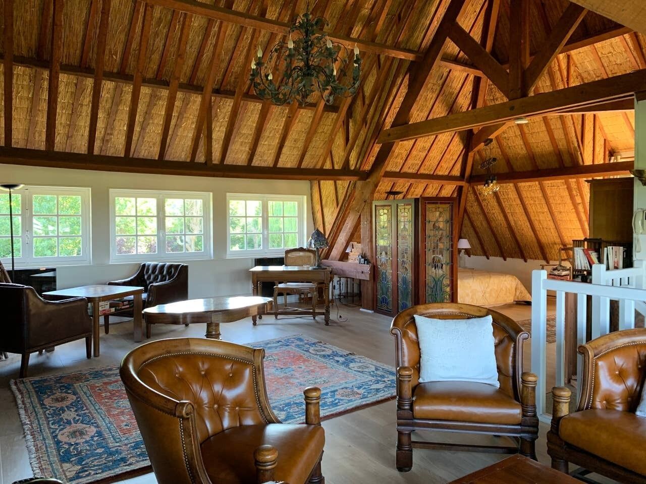 Un loft spacieux avec de hauts plafonds, un grand plafond en bois et un coin salon confortable avec des fauteuils en cuir et un tapis.
