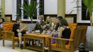Un grupo de personas sentadas en sillas con cojines anaranjados alrededor de una mesa de madera, con una botella de agua y un tazón.