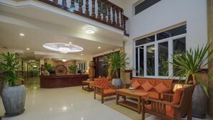 Un amplio vestíbulo con un mostrador de recepción de madera, un área de estar confortable y grandes plantas en macetas.