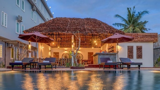 A poolside area with lounge chairs and umbrellas, a thatched roof structure, and a palm tree in the background. - Family room: 1double & single bed - free breakfast (Kok chock commune)