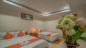 Ein Hotelzimmer mit zwei Betten, einem Nachttisch, einer Lampe, einem gerahmten Bild an der Wand und einer Vase mit Blumen.