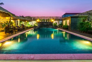 A swimming pool with a stone wall and a thatched roof structure on one side.