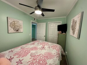 A bedroom with a bed, ceiling fan, artwork, closet, and a television on a shelf. - Gone Coastal! 2 from oceanfront! Central air! (Hilton Head Island)