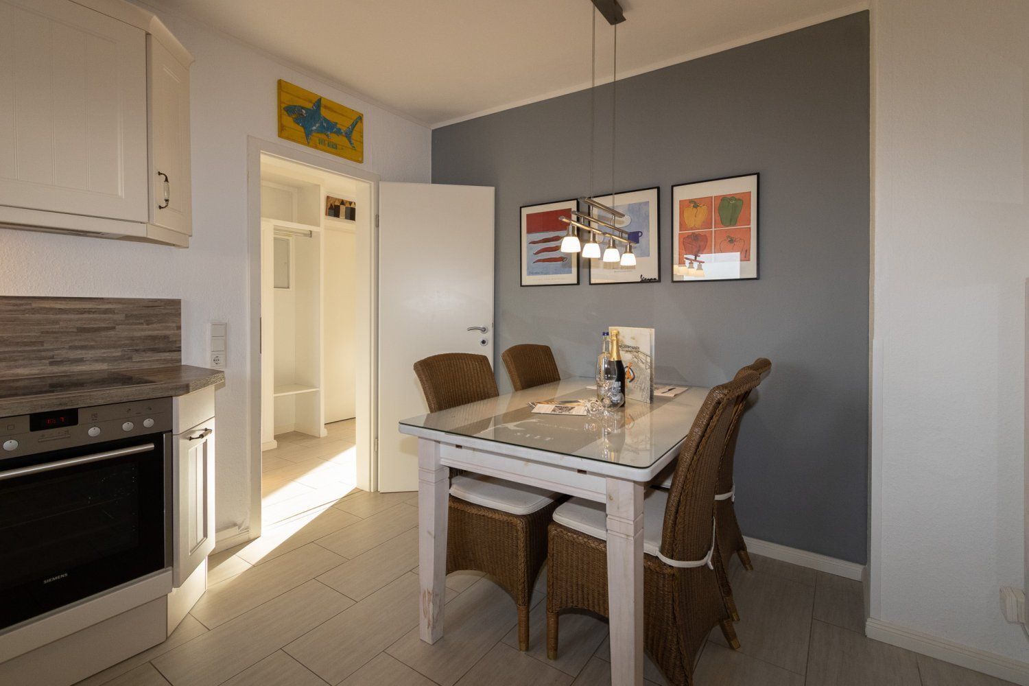 Een moderne keuken met witte kasten, een ingebouwde oven en een eethoek met rieten stoelen en een glazen tafel.