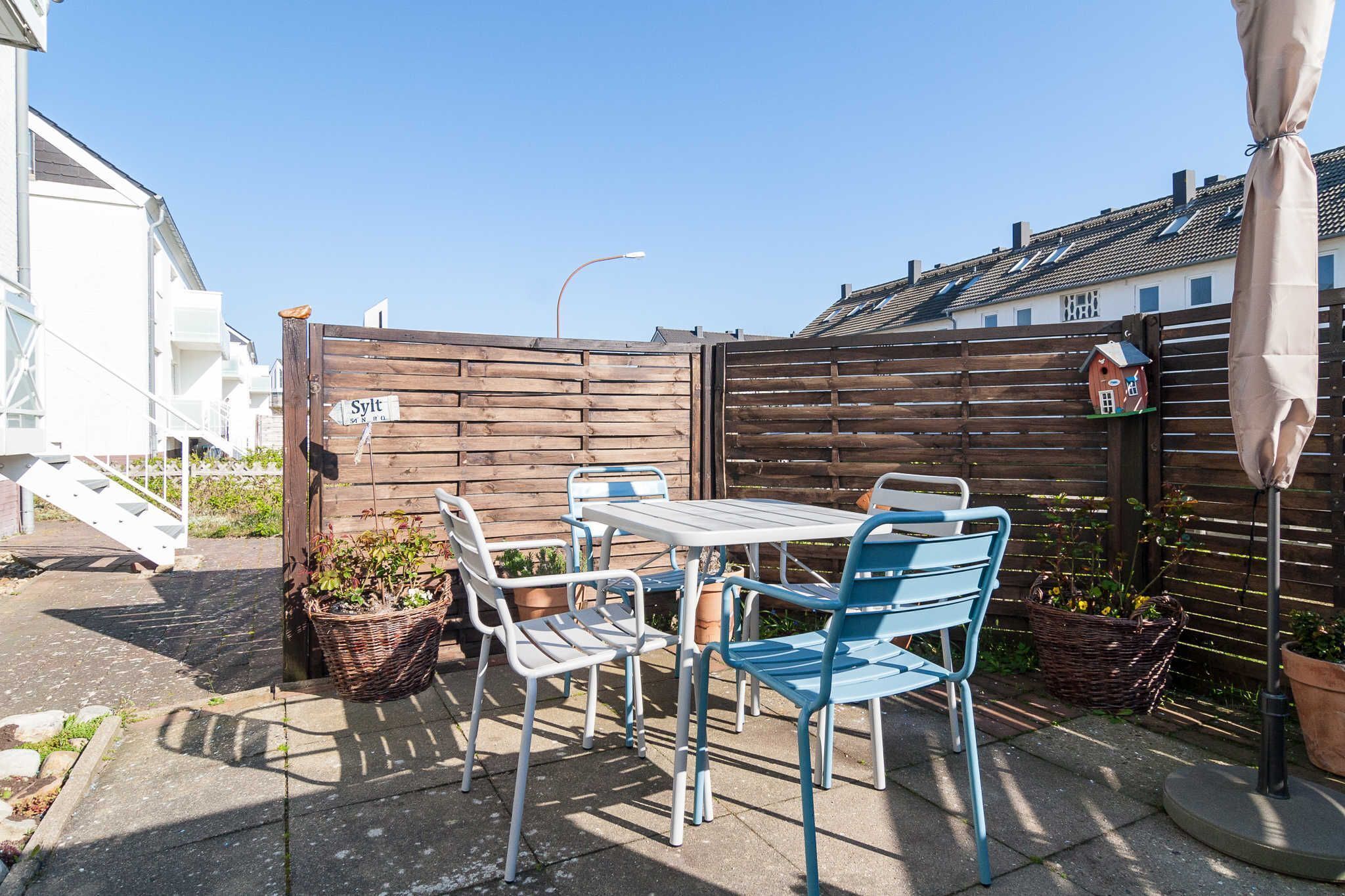 En terrasse med et bord og stole, et træhegn og et gadeskilte.