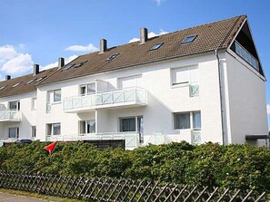 Un immeuble résidentiel de deux étages, à l’extérieur blanc, doté de nombreuses fenêtres et d’un balcon à l’étage supérieur.
