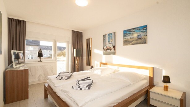 A hotel room with a large bed, a bedside table, a TV, and a window with curtains. - Haus Möwe apartment 5/13 (Hörnum (Sylt))