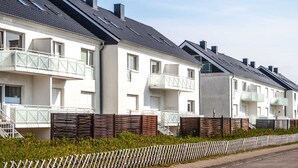 A row of modern, white apartment buildings with balconies and a wooden fence in front. - Haus Möwe apartment 5/13 (Hörnum (Sylt))