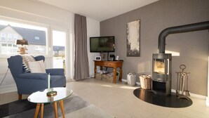 A living room with a sofa, TV, fireplace, and a window with curtains. - Haus Möwe apartment 5/13 (Hörnum (Sylt))