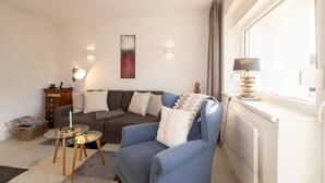 A living room with a sofa, armchair, glass coffee table, and a lamp on a windowsill. - Haus Möwe apartment 5/13 (Hörnum (Sylt))