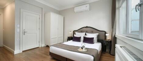 A hotel room with a bed, bedside tables, an air conditioning unit, and a window.