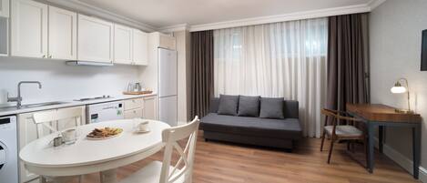 Een moderne keuken met witte kasten, een eettafel met stoelen, een bank en een bureau met lamp.