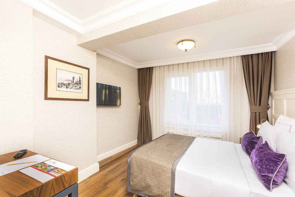 A hotel room with a bed, a desk, a framed picture, and a television.