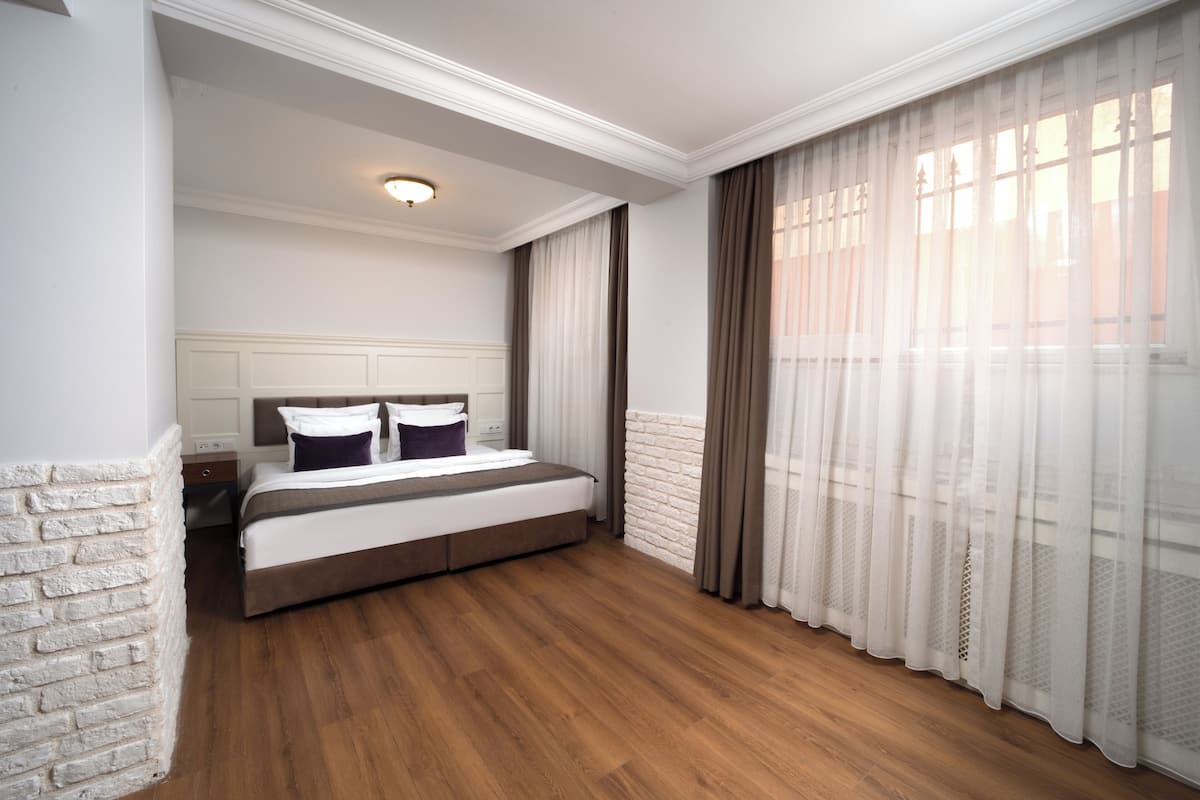 A bedroom with a bed, wooden flooring, a white brick accent wall, and sheer curtains.