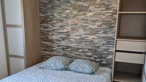 A bedroom with a patterned bedspread, a wooden wardrobe, and a stone-patterned wall.