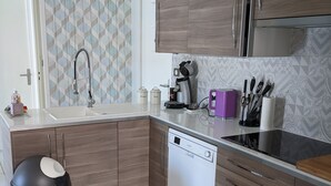 A modern kitchen with wooden cabinets, a dishwasher, a coffee maker, and a trash bin.