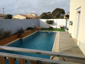 A swimming pool with a wooden deck and a small garden area with a tree and plants.