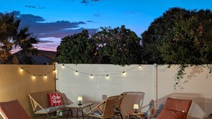 An outdoor patio with lounge chairs, a small table, string lights, and a sign.