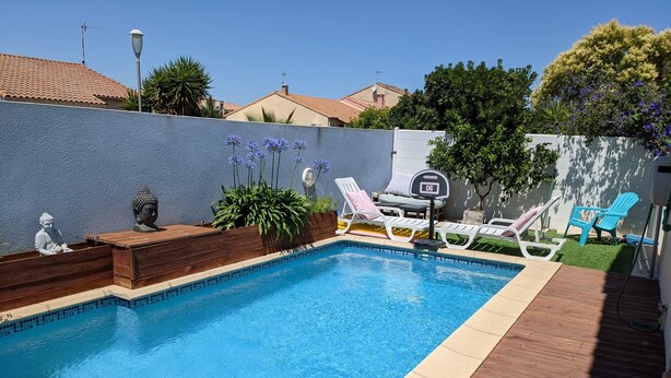 A swimming pool with a wooden deck, lounge chairs, and a Buddha statue.