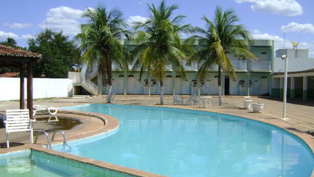 A swimming pool with a tiled edge, surrounded by palm trees and a building with multiple balconies. - Hotel das Palmeiras (Barreiras)