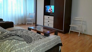 Una camera d'albergo moderna con un letto grande, una TV su un mobile, un pavimento in legno e un ampio armadio.