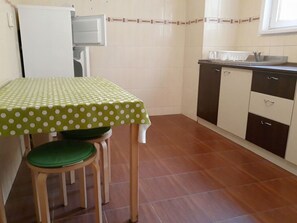 A small kitchen with a table and two chairs, a refrigerator, a sink, and cabinets.