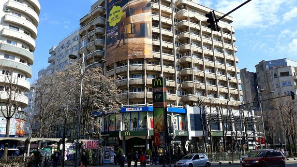 Un edificio a più piani con un grande cartellone pubblicitario su un lato, un ristorante McDonald's e una fermata dell'autobus.