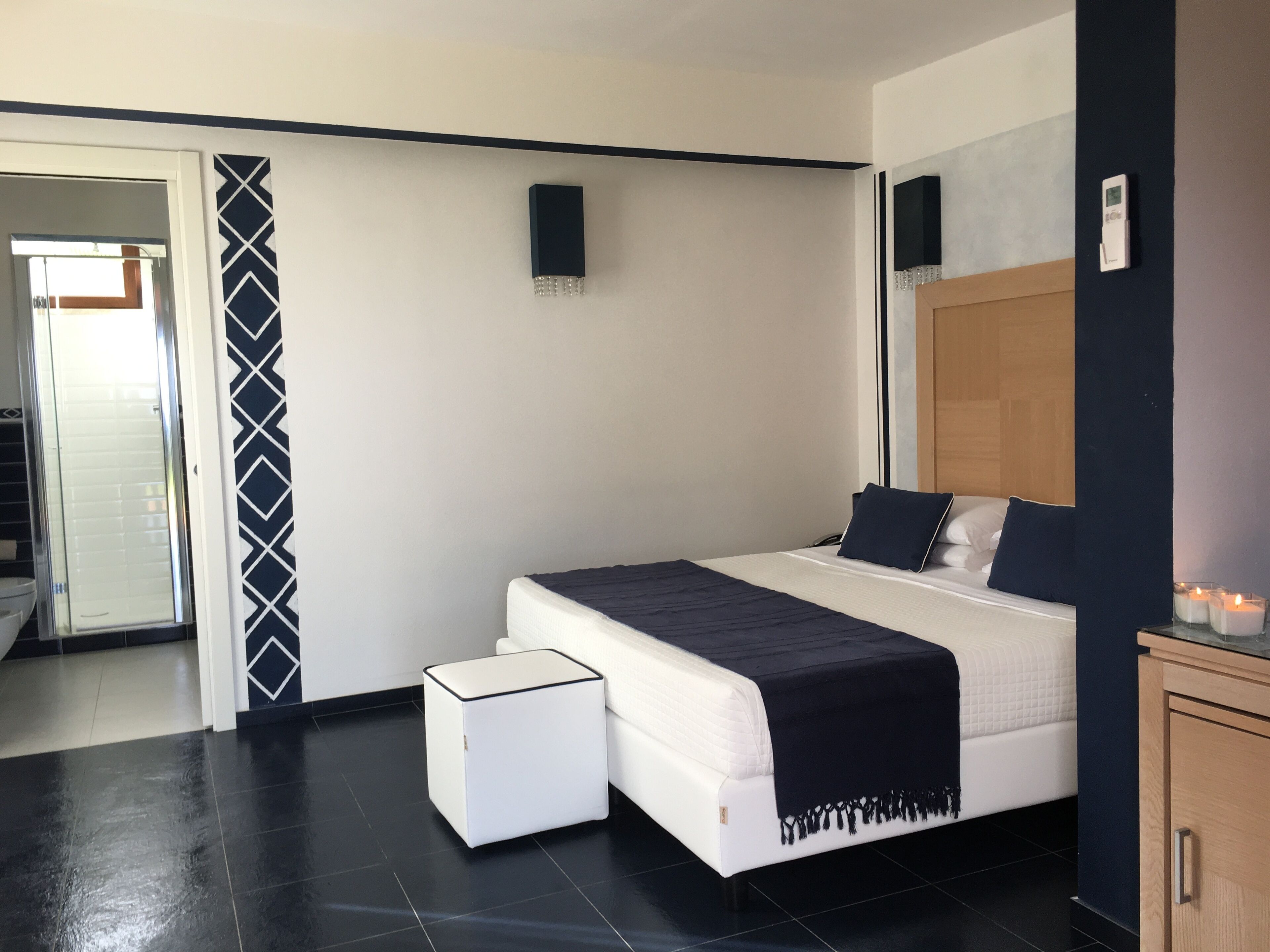 Un dormitorio moderno con una cama grande, una mesita de noche pequeña, un armario y un baño visible a través de una puerta abierta.
