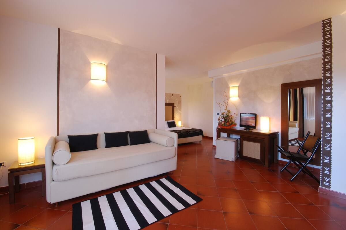 A modern living room with a white sofa, a black and white striped rug, a small table with a lamp, and a TV on a stand.