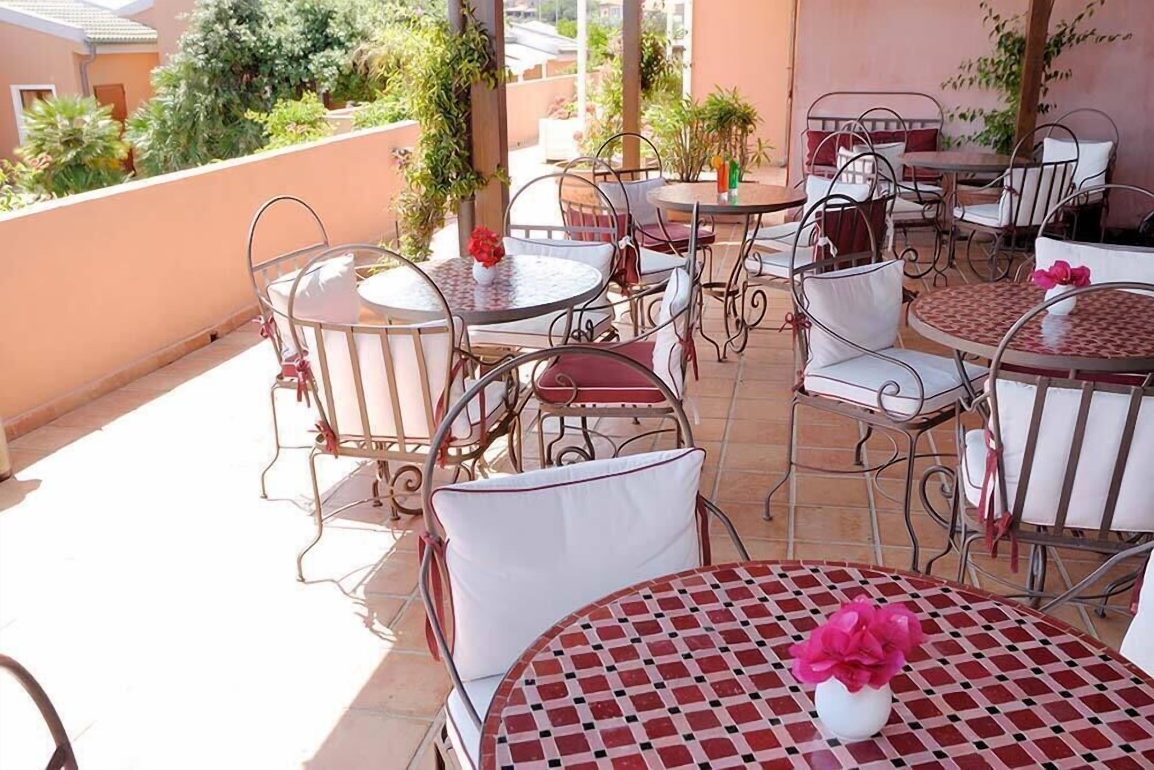 Una terrazza con tavoli e sedie rotonde, alcune con cuscini bianchi e altre con cuscini rossi.