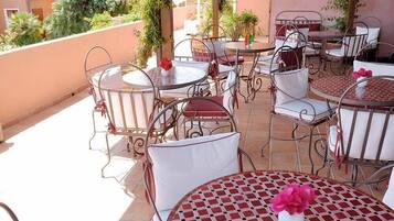 Una terrazza con tavoli e sedie rotonde, alcune con cuscini bianchi e altre con cuscini rossi.