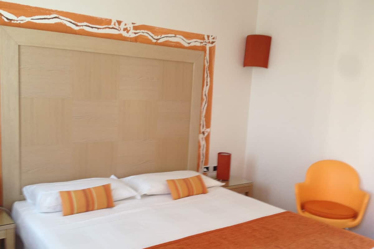 A hotel room with a large bed, a wooden headboard, a chair, and a red wall decoration.