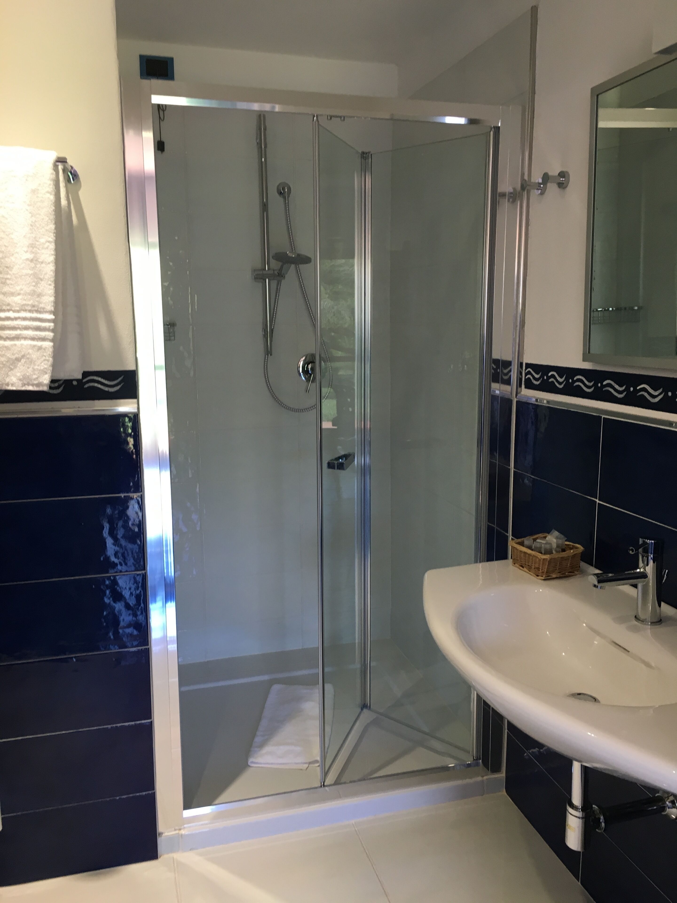 A modern bathroom with a glass-enclosed shower, a white sink, and dark blue tiled walls.