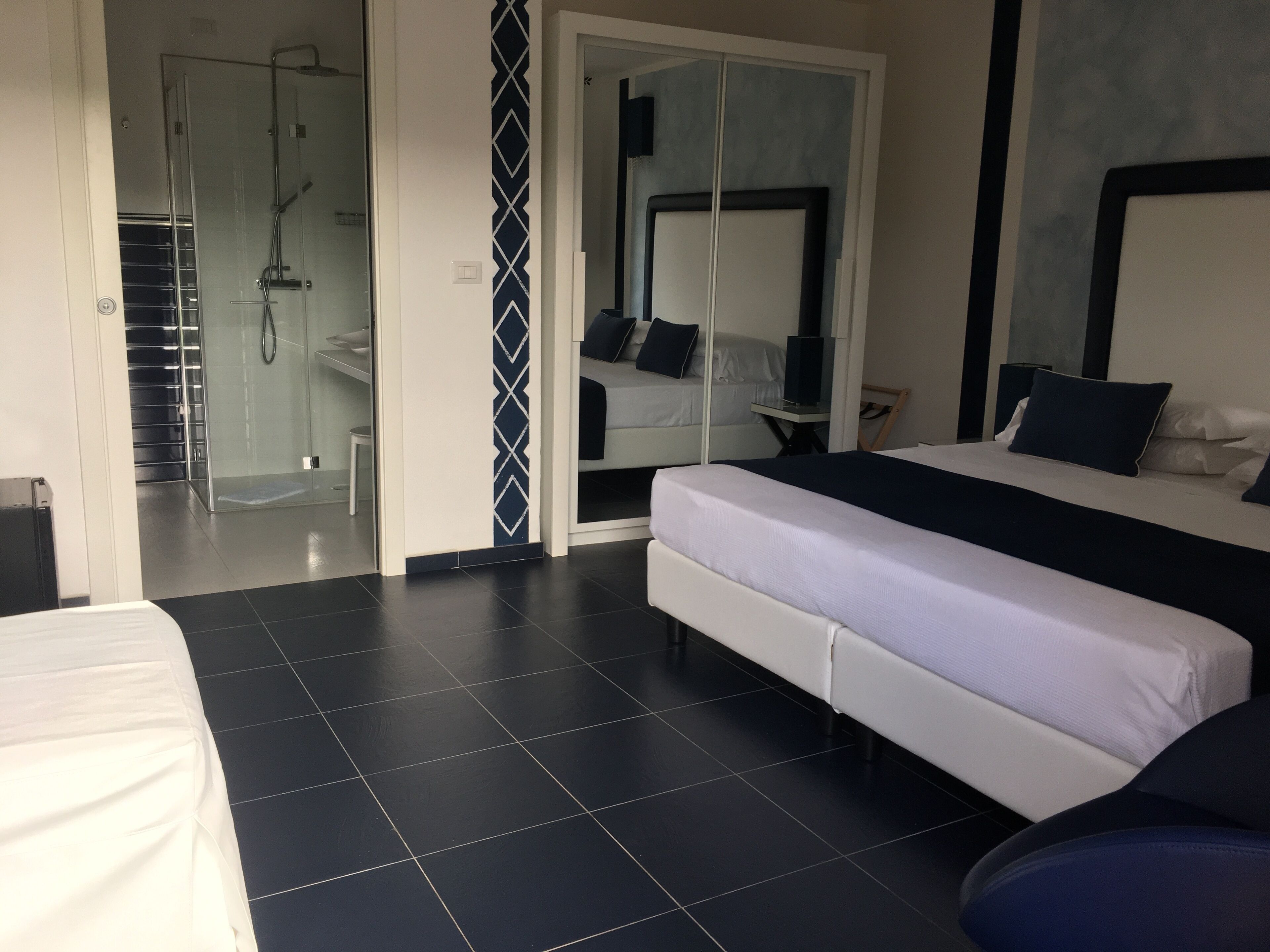 A modern hotel room with a large bed, a separate seating area, a glass-enclosed shower, and a large mirror.