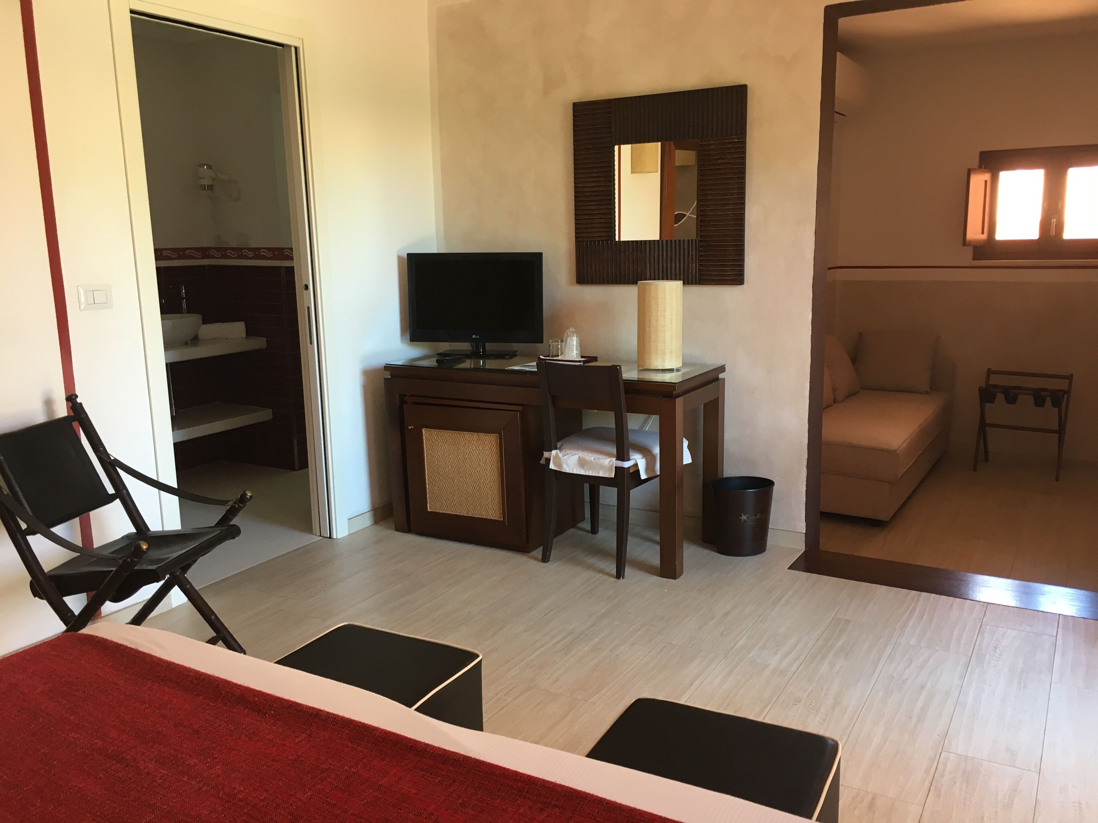 Una habitación de hotel con una cama, un escritorio con computadora, una silla, un sofá y una mesita de noche con lámpara.