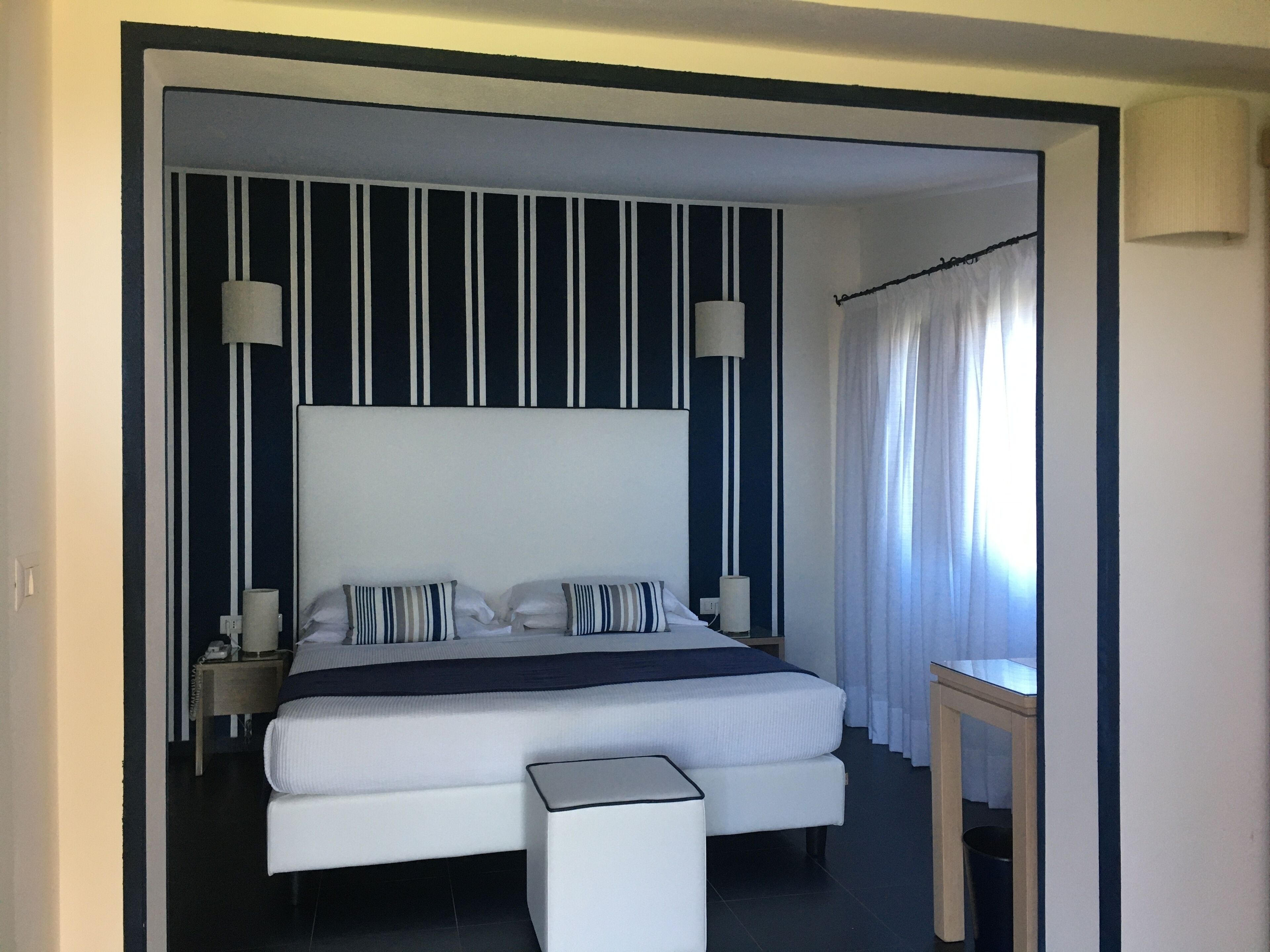 A modern hotel room with a large bed, striped wall panels, and a bedside table with a lamp.